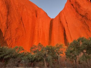 Up close to Uluru the sheer cliffs glow bright red in the evening light.